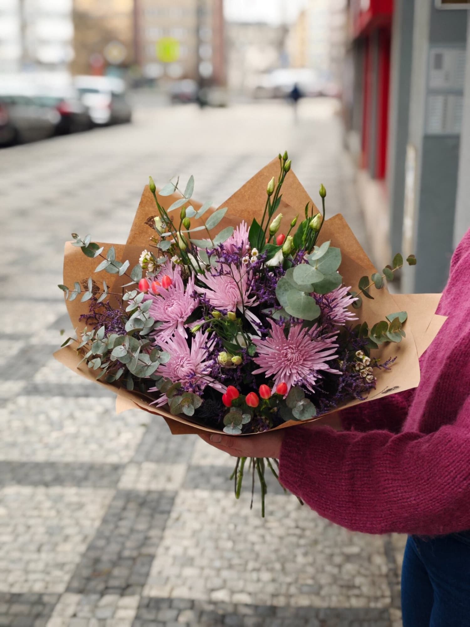 Kytice s fialovými chryzantémami v ruce na pražské ulici